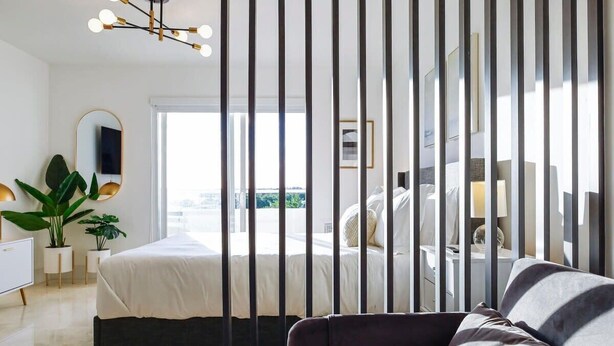 Ein modernes Schlafzimmer mit einem großen Bett, einer dunklen Couch, einem Nachttisch, einem Spiegel und einer Topfpflanze.