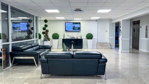 Eine moderne Lobby mit einem schwarzen Ledersofa, einem Flachbildfernseher und einer Rezeption.