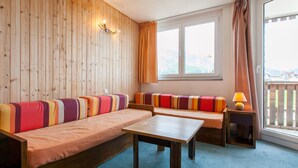 A cozy room with a wooden wall, a sofa with colorful cushions, a small table, and a window with curtains.