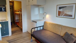 Et lille værelse med køjeseng, skrivebord med computer, lille tekøkken og enkeltseng med pude.
