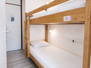 Un lit superposé avec une structure en bois, une literie blanche et un luminaire placé au-dessus du lit supérieur.