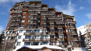 Et hotel med flere etager, altaner, en skiskole og et sneklædt tag.