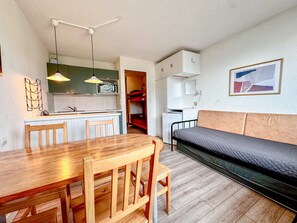 A compact living space with a kitchenette, a dining area with a wooden table and chairs, a sofa, and a bed. - Central Avoriaz studio with balcony for 4 people (Avoriaz)
