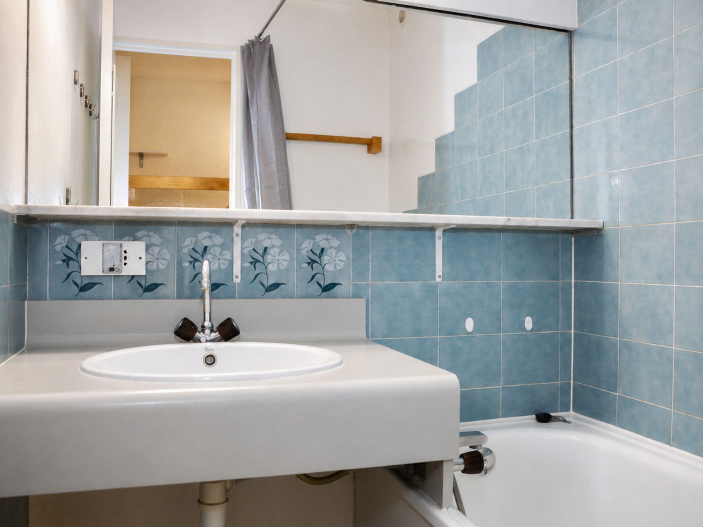 Ein Badezimmer mit einem weißen Waschbecken, einem Spiegel darüber und blautonierten Fliesen.