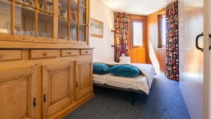 A bedroom with a wooden cabinet, a bed with blue pillows, and patterned curtains.