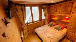 A cozy wooden room with a bed, a TV mounted on the wall, and a window with curtains.