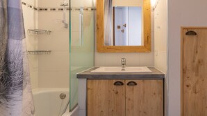 A bathroom with a glass shower enclosure, a wooden vanity with a mirror, and a bathtub.