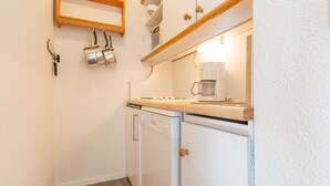 Ett kompakt kök med diskmaskin, kaffebryggare och en hylla i trä ovanför bänkskivan.