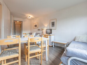 A room with a dining table, chairs, a bed, a desk with a lamp, and a telephone.