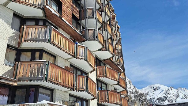 Un hôtel à plusieurs étages, doté de balcons en bois et d’une façade en pierre, qui se dresse sur fond de montagnes enneigées.