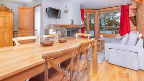 Een knus interieur met een houten eettafel, stoelen, een grijze bank en een stenen open haard.