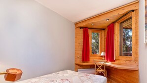 Een gezellige slaapkamer met een houten plafond, een bed met een bloemenquilt, een bureau met een lamp en een raam met rode gordijnen.