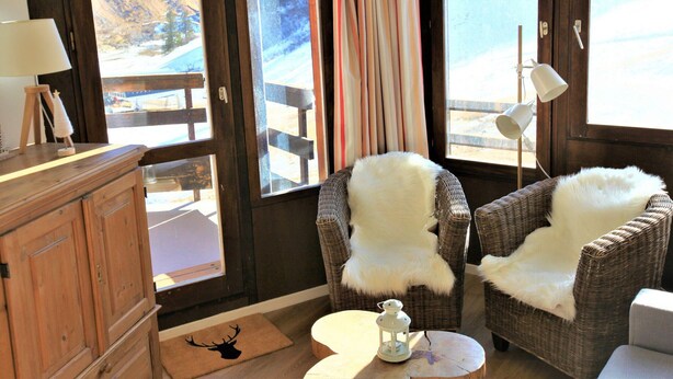 A cozy room with wicker chairs, a wooden cabinet, and a view of a snowy landscape through large windows.