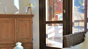 A wooden cabinet with a lamp, a wicker chair, and a view of a mountainous landscape through a window.