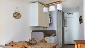 A modern kitchen with white cabinets, a wooden dining table, and a hanging light fixture.