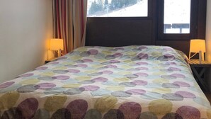 A bedroom with a bed, two bedside lamps, a window with a view of a snowy landscape, and a curtain.