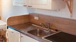 A compact kitchen with white cabinets, a stainless steel sink, and a microwave.