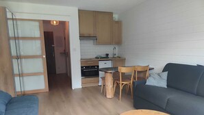 A compact living space with a kitchenette, a dining area, and a seating area with a sofa and a small round table.