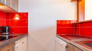 Una cocina compacta con baldosas rojas, una tetera de acero inoxidable y un lavavajillas.