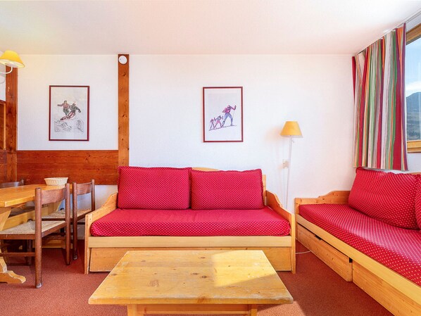 Une pièce chaleureuse avec un canapé en bois, une table en bois et un banc en bois. Deux tableaux encadrés sont accrochés au mur.