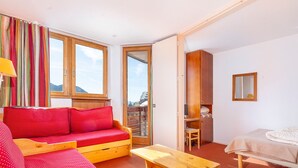 Una habitación con un sofá rojo, una mesa de madera, una cama, un escritorio y una ventana con cortinas.