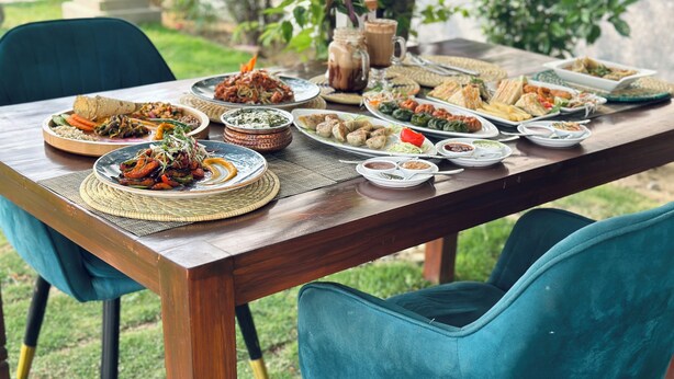 A wooden dining table set outdoors with various dishes and a pitcher of iced tea. - Lumbini Five Elements Hotel (Lumbini)