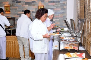 Montaje de bufé con varias estaciones de comida y personas sirviéndose.