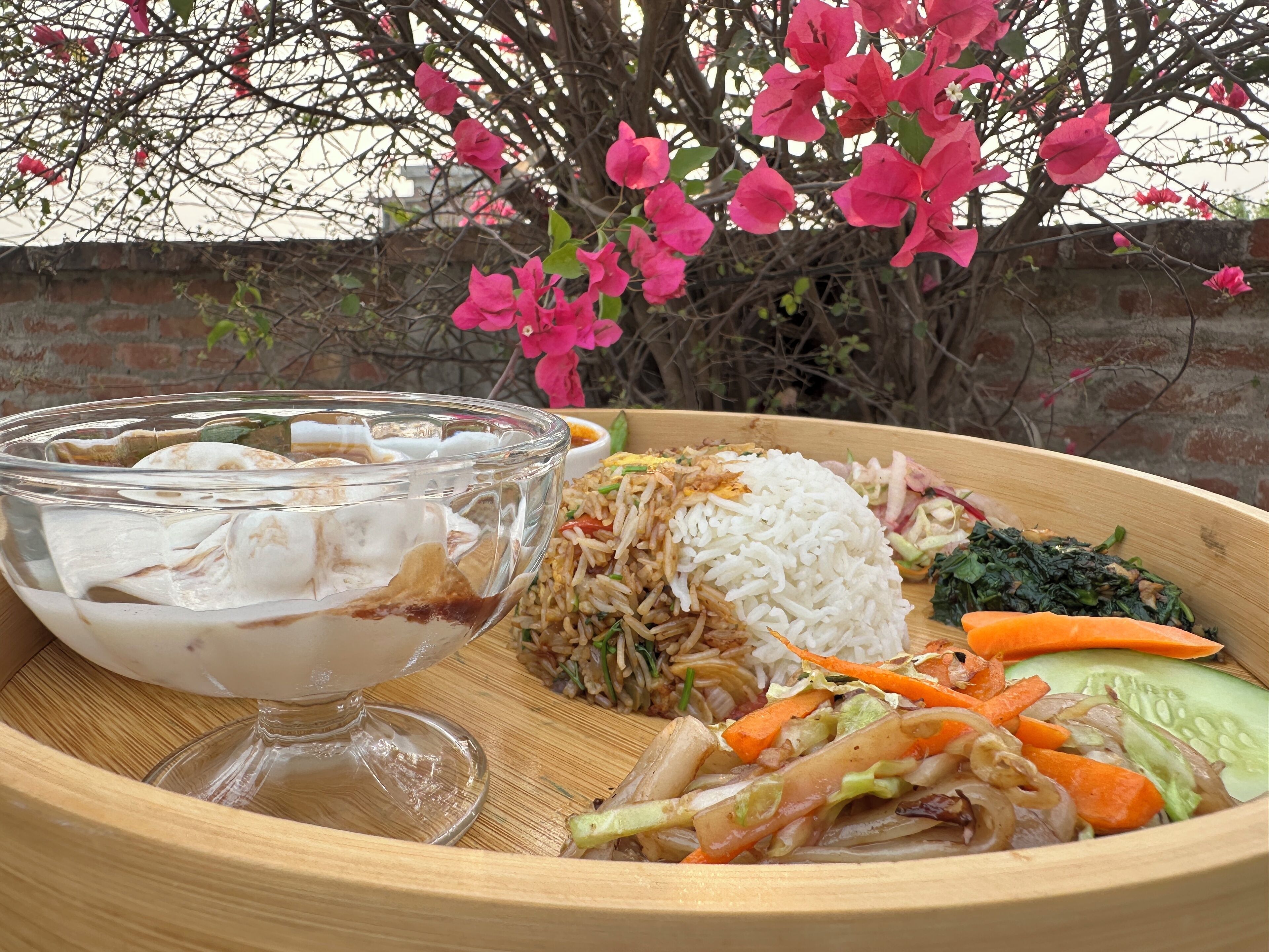 A wooden tray with a bowl of soup, a plate of rice, vegetables, and a piece of meat.