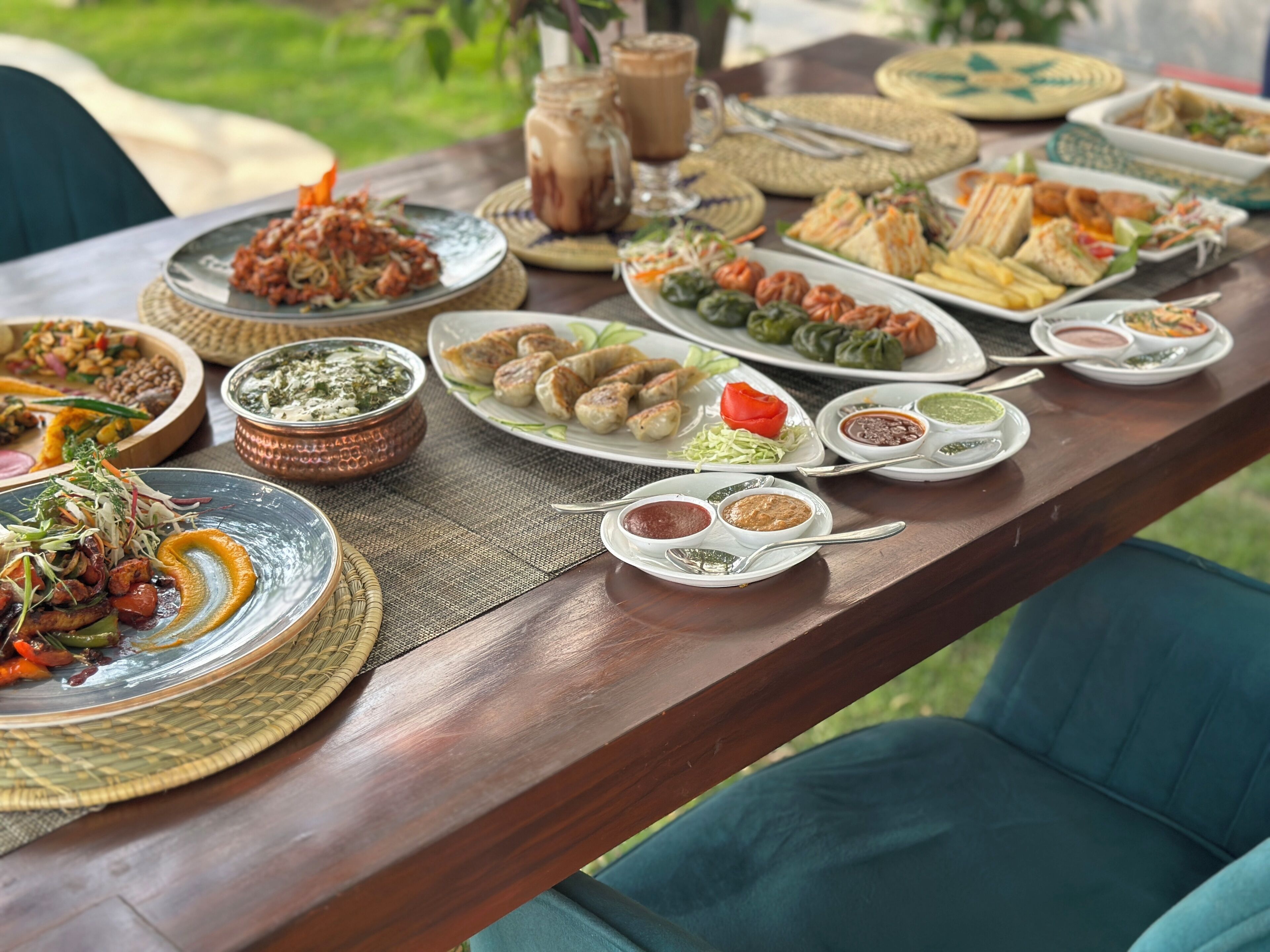 Ein Holztisch, reichhaltig gedeckt mit verschiedenen Speisen, darunter Salate, Fleischgerichte und Desserts, was auf ein Buffet hindeutet.