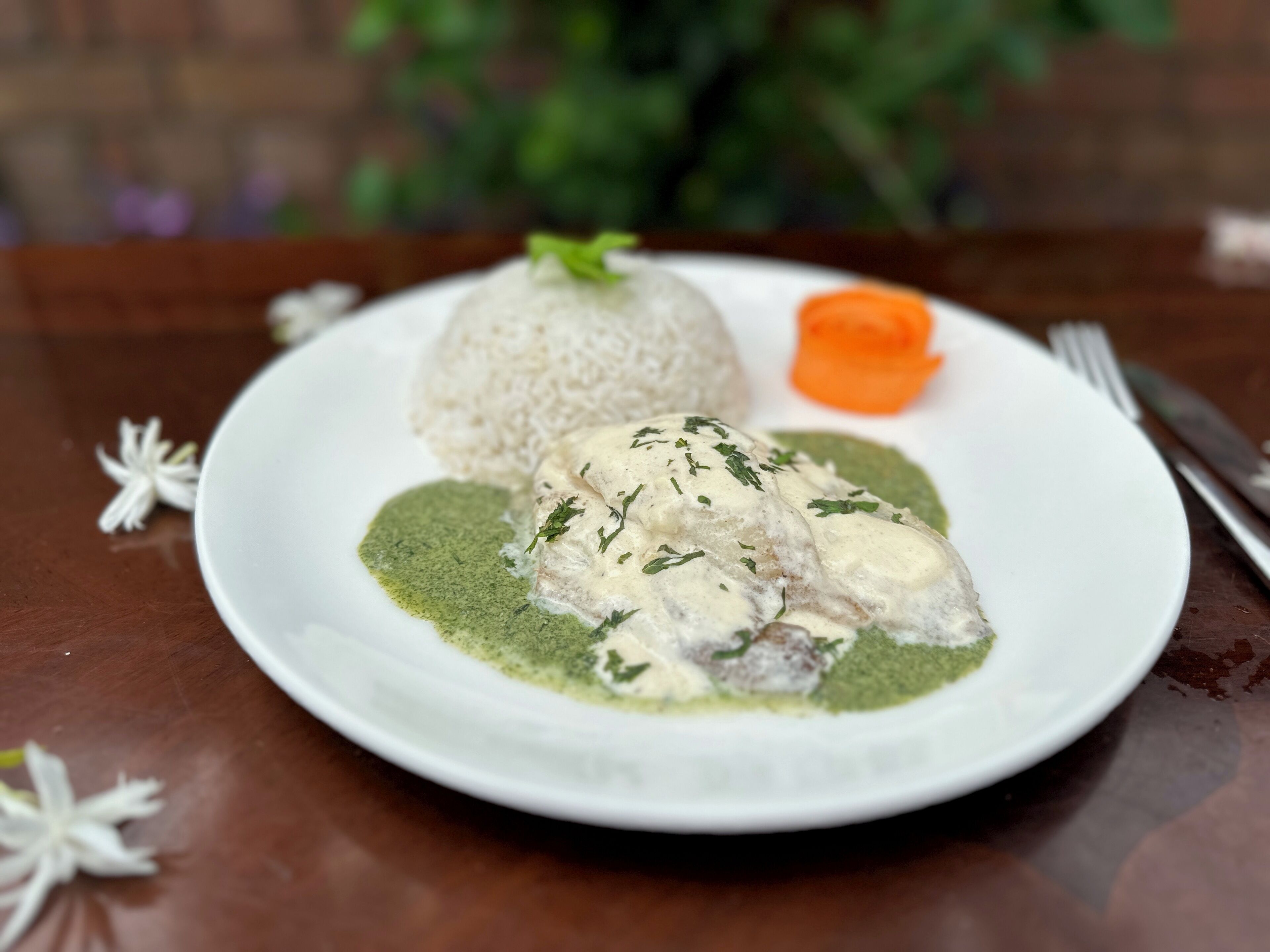 A plate with a white rice mound, a piece of meat with a creamy sauce, and a green sauce.