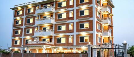 A multi-story hotel with balconies, a gated entrance, and a well-lit facade.