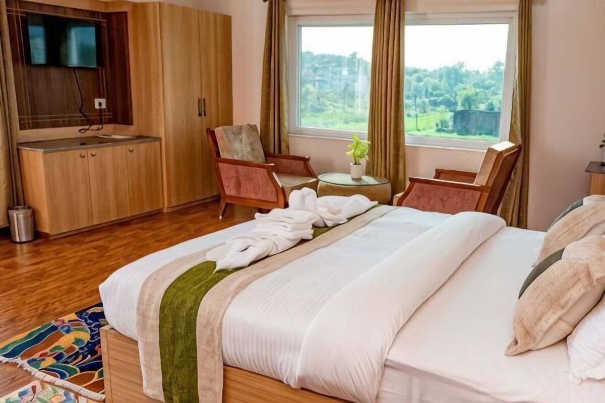 A hotel room with a bed, a small kitchenette, a TV, a window with a view, and a chair.