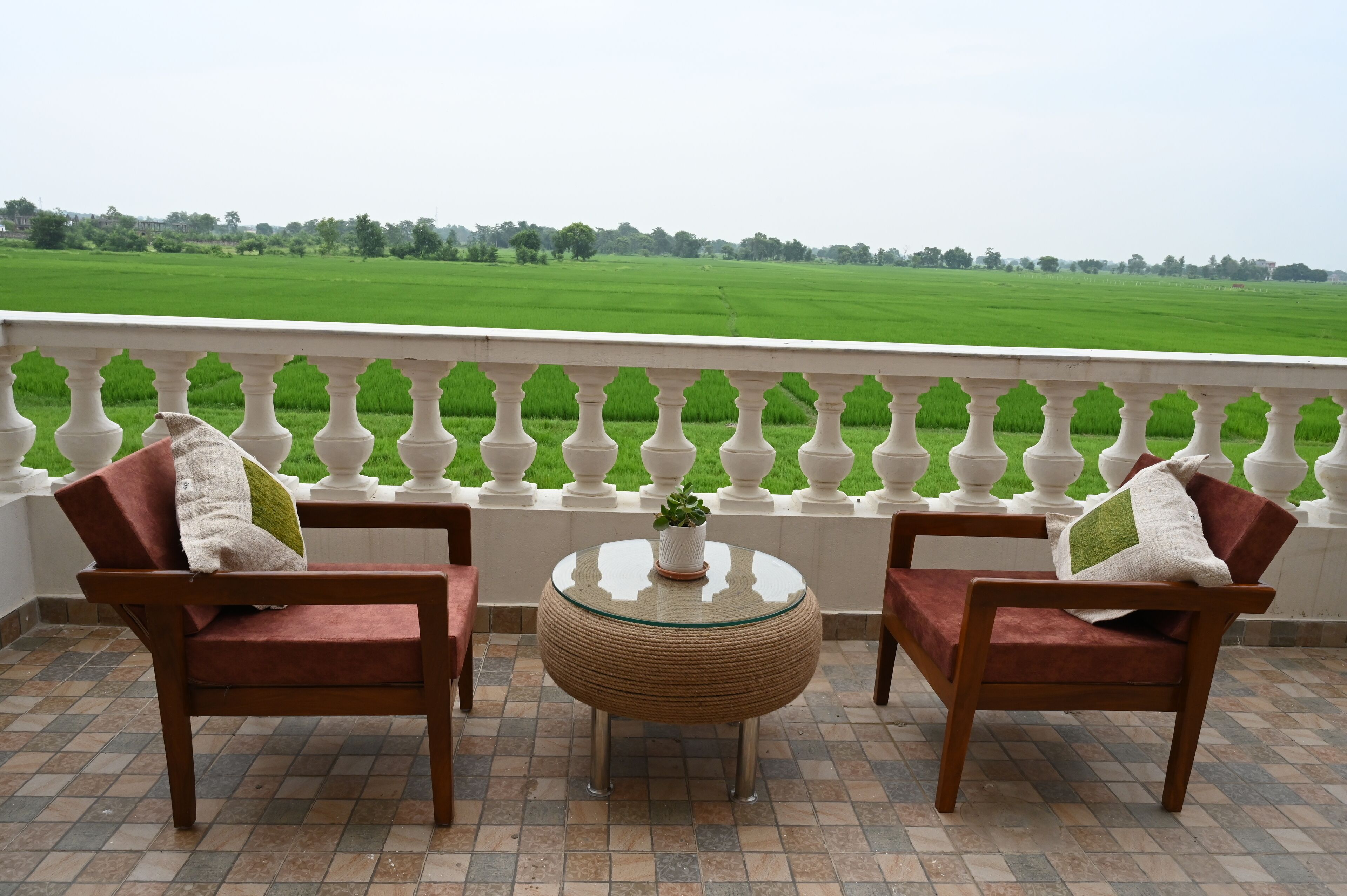 A balcony with two wooden chairs and a round table, overlooking a green field.