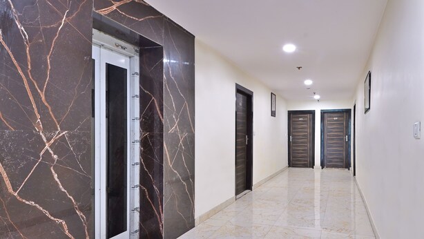 A hallway with marble walls and floors, featuring a door with a nameplate and a door with a number plate. - Hotel Hari International (Noida)