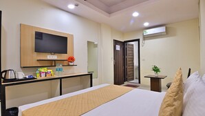 A hotel room with a bed, a TV mounted on the wall, a small table with snacks and drinks, a mirror, and a door with a sign. - Hotel Hari International (Noida)