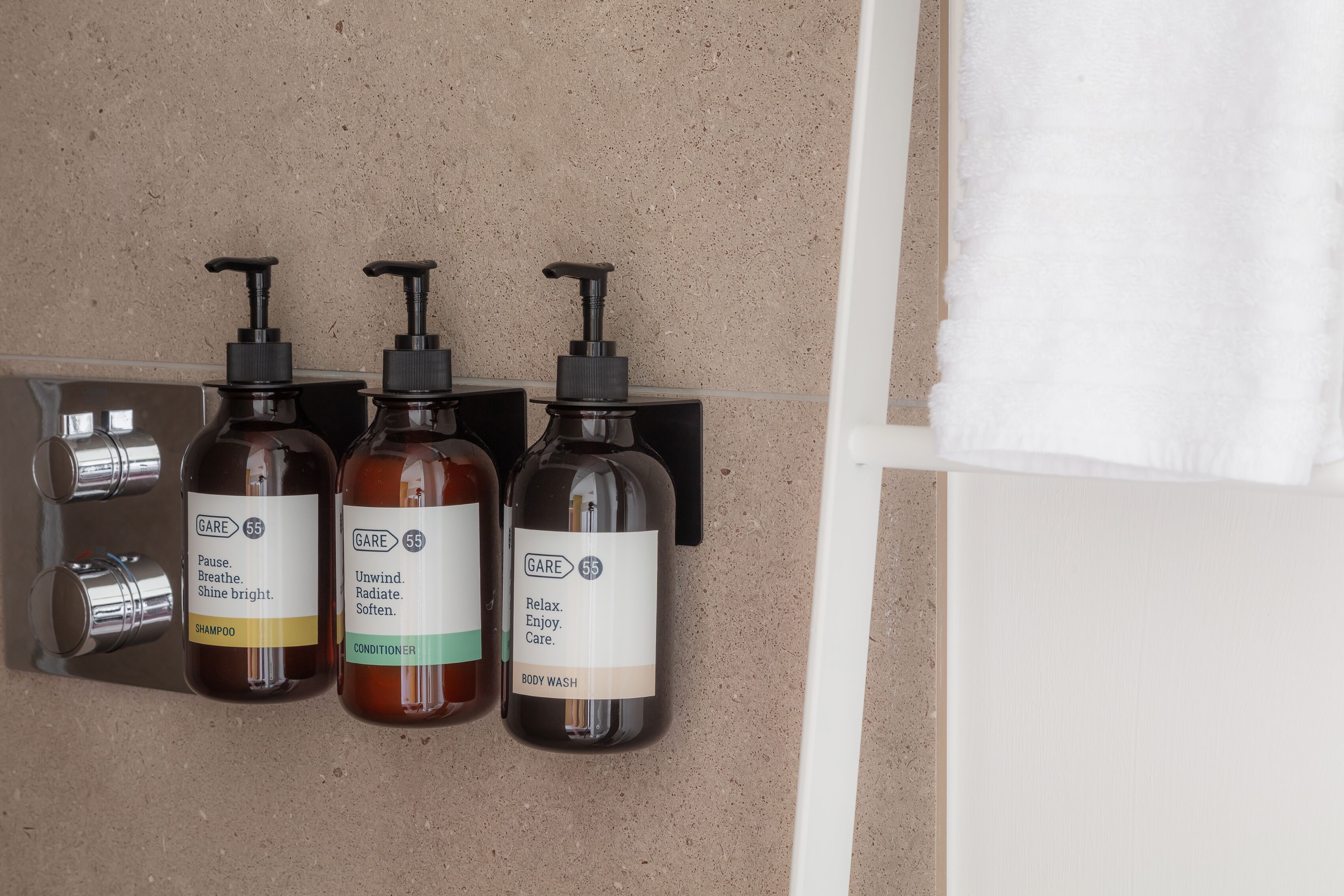 Three bottles of GARE body wash, shampoo, and conditioner on a wall-mounted dispenser.