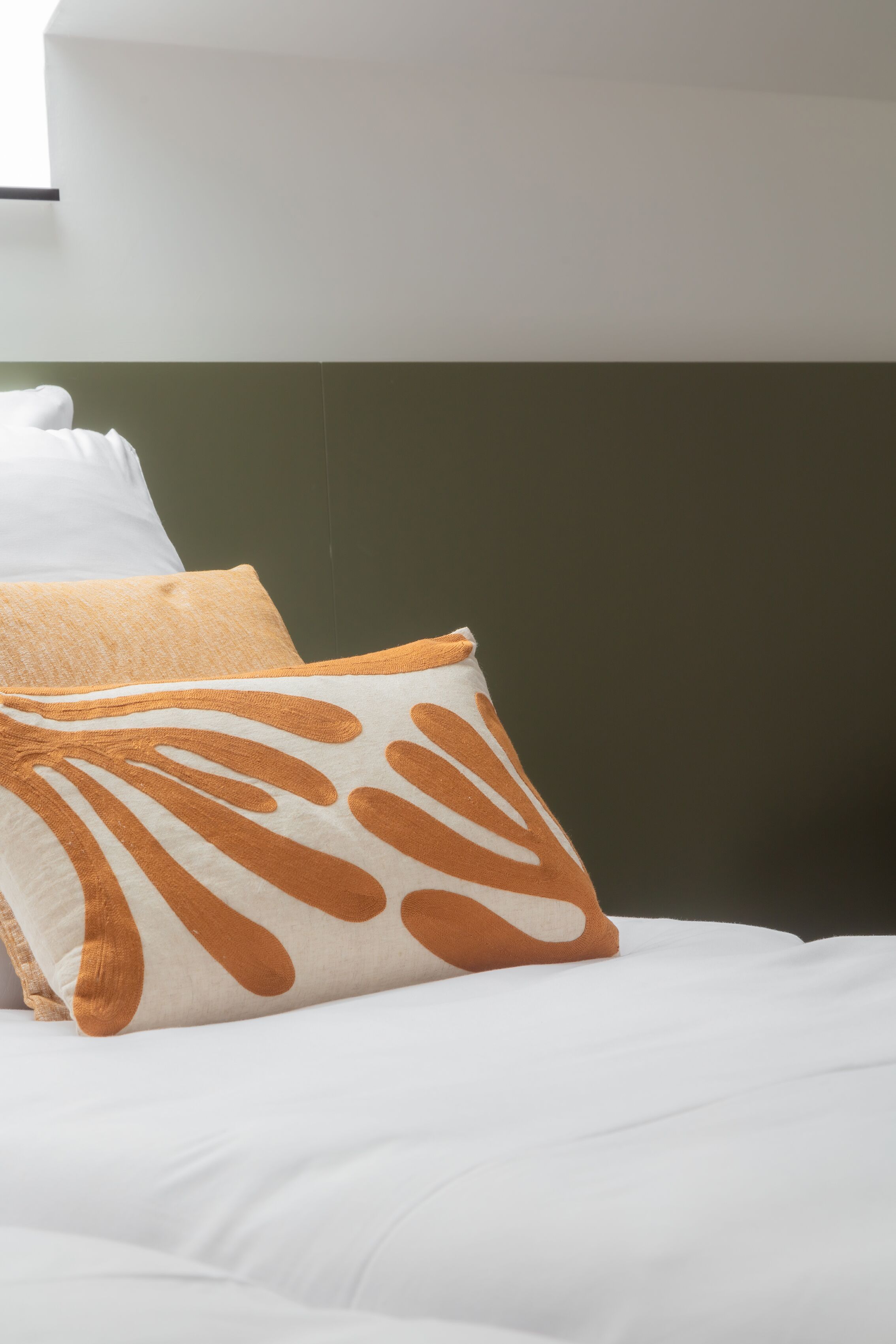Una cama con ropa de cama blanca y dos almohadas, una con estampado de hojas y la otra lisa.