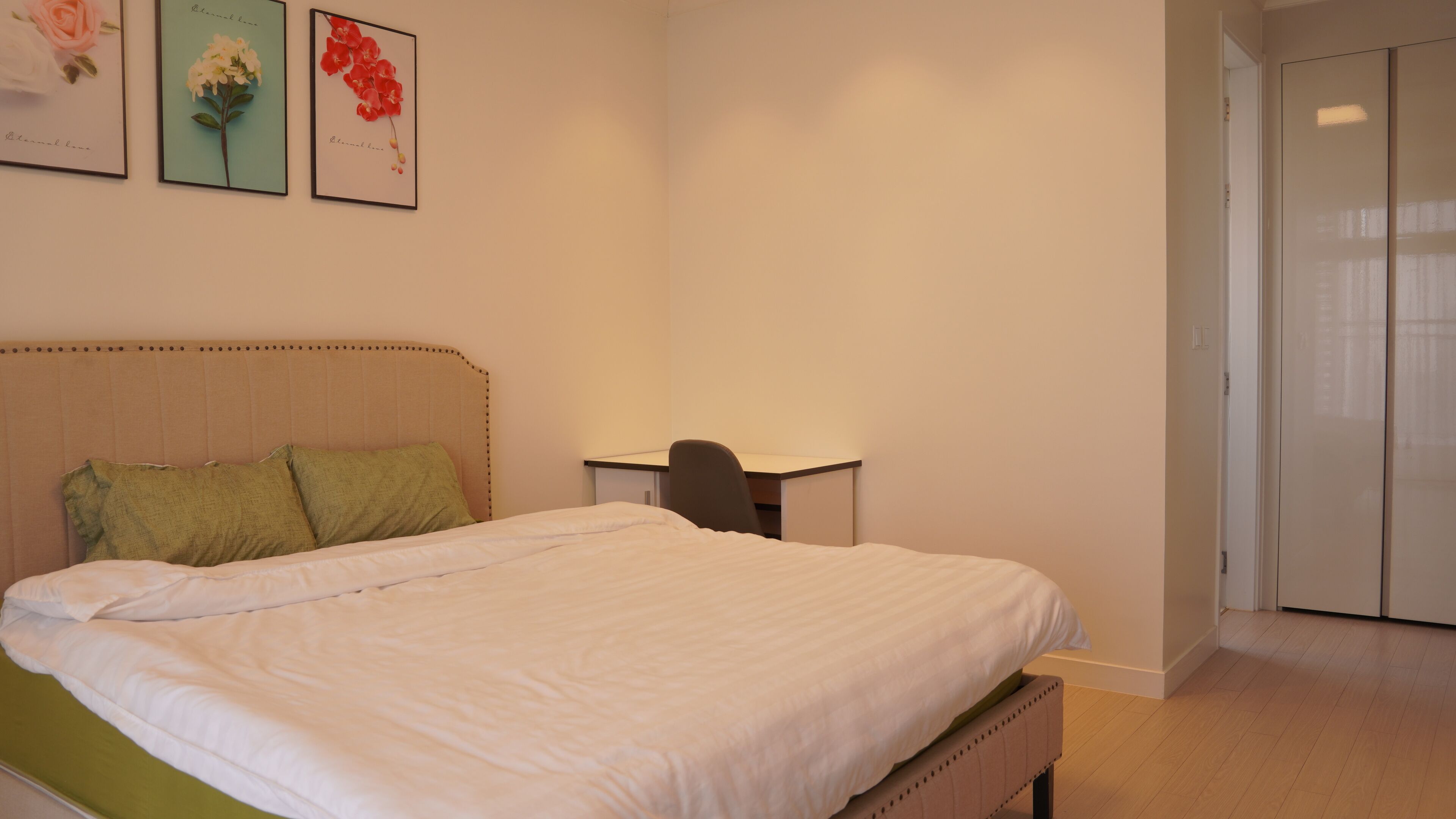 A bedroom with a bed, a desk, and a chair. There are two framed pictures on the wall.
