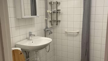 A small, compact bathroom with a white sink, a wooden toilet, a shower with a grey curtain, and a mirror above the sink.