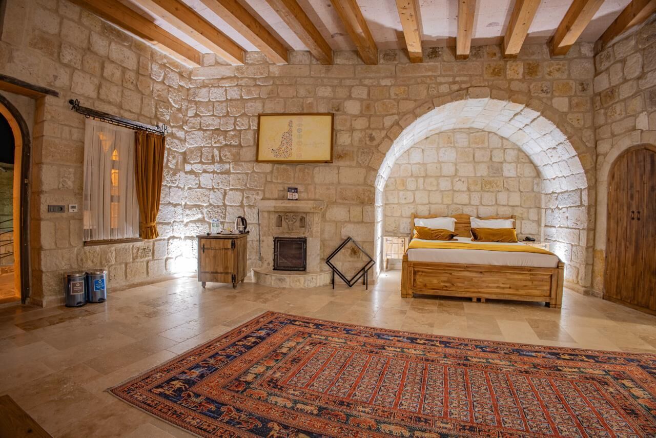 A stone-walled bedroom with a large bed, a fireplace, and an arched doorway.