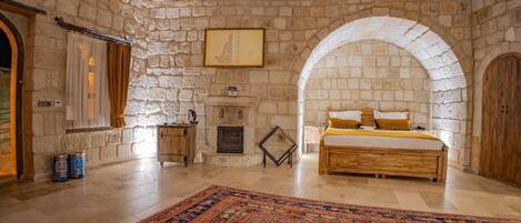 A stone-walled bedroom with a large bed, a fireplace, and an arched doorway.