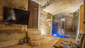A stone-walled room with a wooden staircase, a flat-screen TV, and a glass-enclosed pool area. - Chakra Special Caves (Ürgüp)