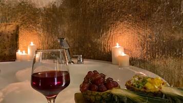 A table with a wine glass, grapes, and a pineapple on a white countertop, surrounded by candles.