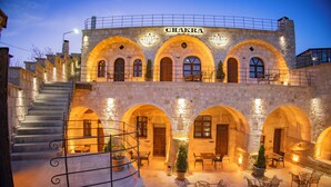 A stone building with the name "CHAKRA" illuminated at the top. It features multiple arched doorways, outdoor seating areas, and a staircase leading to an upper level. - Chakra Special Caves (Ürgüp)
