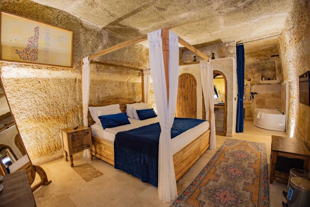 A stone-walled bedroom with a four-poster bed, a wooden nightstand, and a large rug.