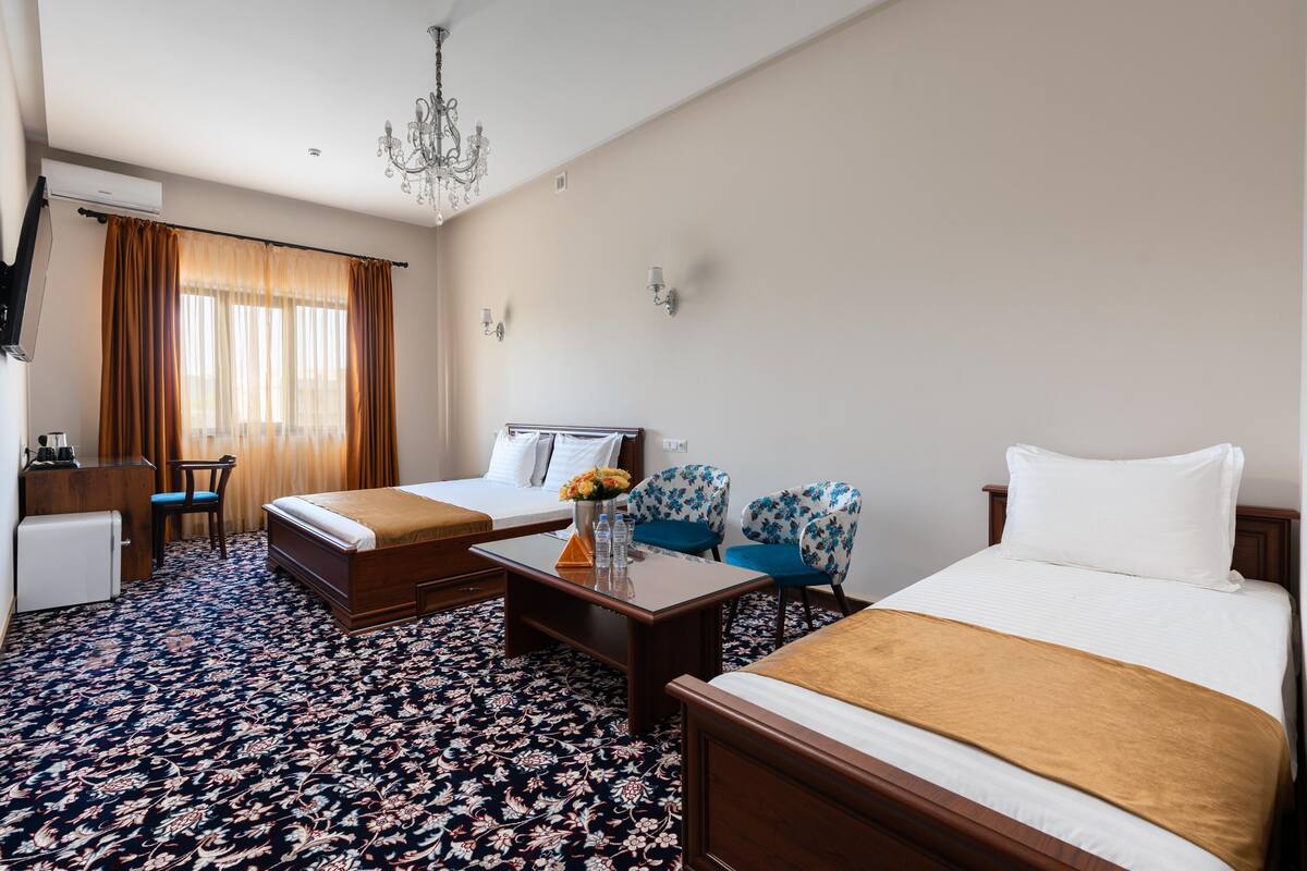 A hotel room with two beds, a desk, a chair, a coffee maker, and a chandelier.
