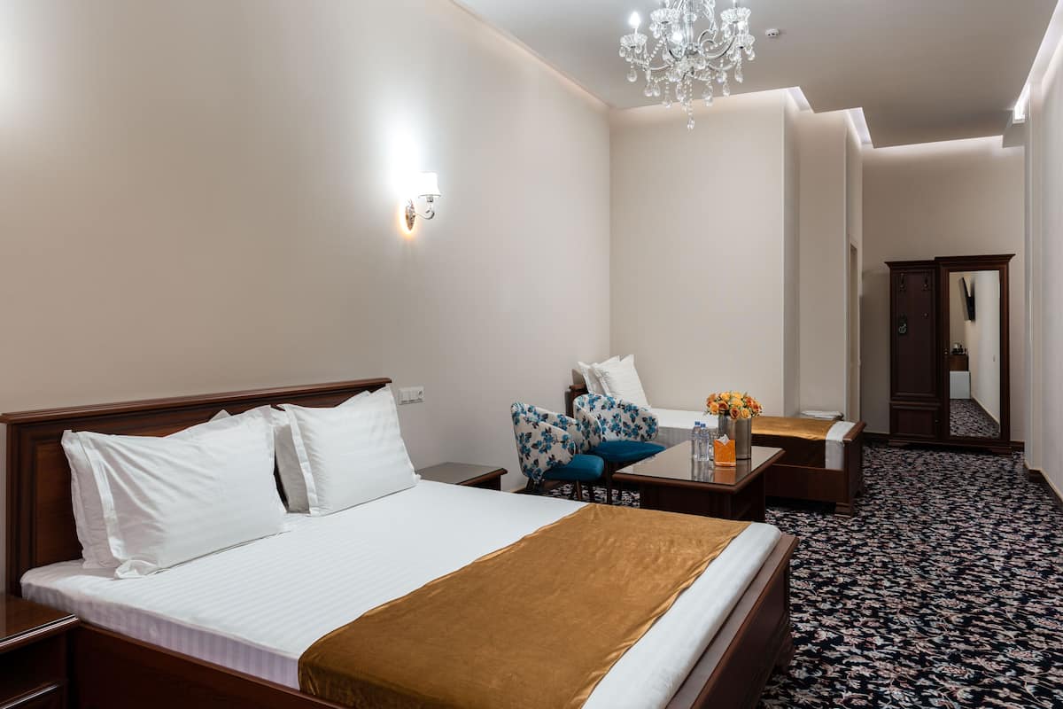 A hotel room with a large bed, a bedside table with a vase of flowers, a chair, and a mirror.