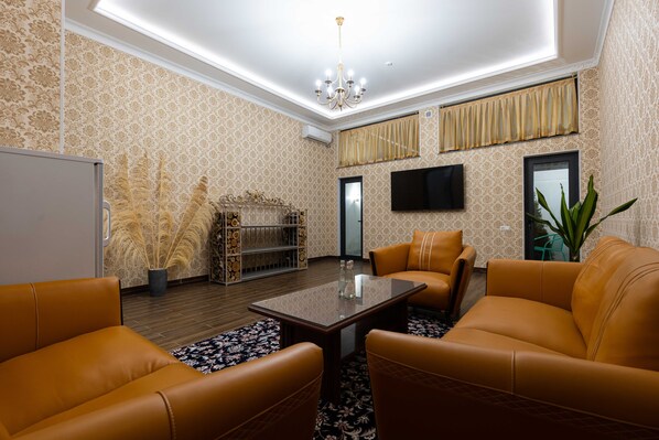Ein modernes Wohnzimmer mit Ledersofas, einem Glastisch und einem an der Wand befestigten Fernseher.