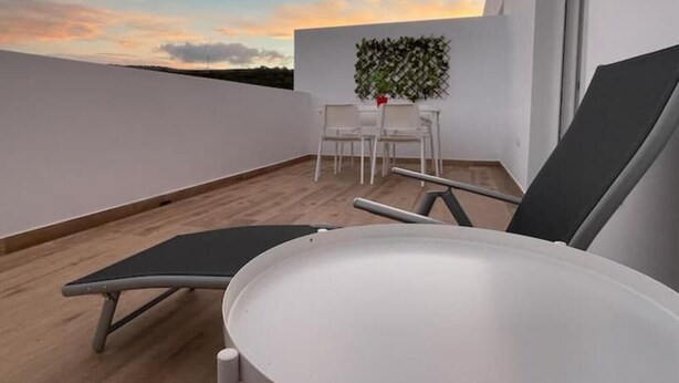 Une terrasse sur le toit, avec une table et des chaises, un pot de fleurs et une vue sur le coucher de soleil.