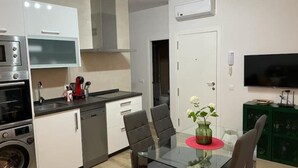 Une cuisine moderne équipée d’un four à micro-ondes, d’un four traditionnel et d’un lave-vaisselle, un coin repas avec une table et des chaises en verre, et un téléviseur fixé au mur.